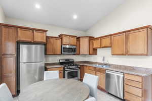 Kitchen with stainless steel appliances, lofted ceiling, brown cabinetry, and recessed lighting