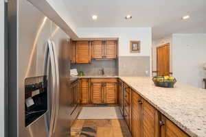 Kitchen featuring brown cabinets, stainless steel appliances, backsplash, light stone counters, and recessed lighting