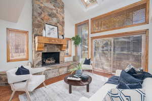 Living area with high vaulted ceiling, wood finished floors, a stone fireplace, and a skylight