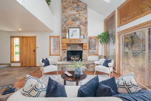 Living area featuring high vaulted ceiling, a fireplace, wood finished floors, and a skylight
