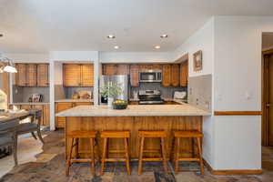Kitchen featuring tasteful backsplash, a breakfast bar, brown cabinetry, light stone countertops, and stainless steel appliances