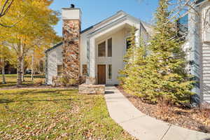 View of front door of property with a chimney and a front lawn