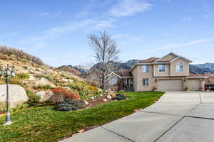 Traditional-style house featuring a mountain view, concrete driveway, a garage, a front yard, and stucco siding