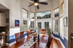 Dining area with dark wood-type flooring, a towering ceiling, a ceiling fan, and plenty of natural light