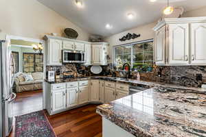 Kitchen featuring vaulted ceiling, stainless steel appliances, dark wood-type flooring, backsplash, and tile counters