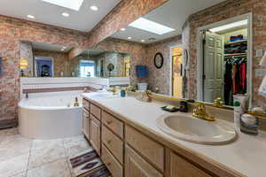 Full bathroom with double vanity, a skylight, light tile patterned floors, a walk in closet, and a garden tub