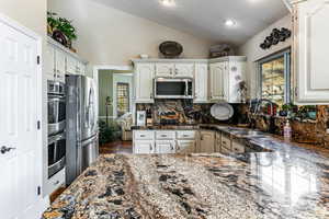 Kitchen featuring vaulted ceiling, healthy amount of natural light, appliances with stainless steel finishes, white cabinetry, and recessed lighting