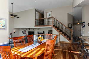 Dining room featuring dark wood-type flooring, stairs, a towering ceiling, and a ceiling fan