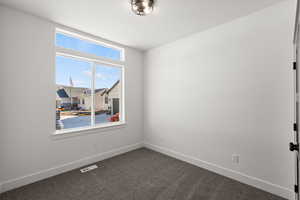 Spare room featuring dark carpet and baseboards