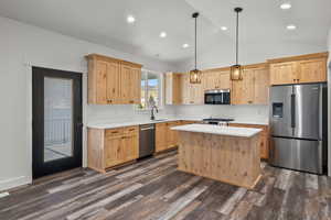 Kitchen featuring light brown cabinets, appliances with stainless steel finishes, lofted ceiling, dark wood-style floors, and a kitchen island