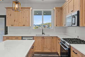 Kitchen featuring light brown cabinetry, appliances with stainless steel finishes, light stone counters, pendant lighting, and dark wood-type flooring