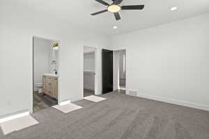 Unfurnished bedroom with dark colored carpet, a spacious closet, ensuite bathroom, recessed lighting, and ceiling fan
