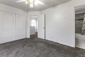 Unfurnished bedroom featuring dark colored carpet, a closet, ceiling fan, and connected bathroom