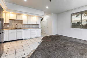 Kitchen featuring light tile patterned flooring, tasteful backsplash, white cabinets, white dishwasher, and light colored carpet