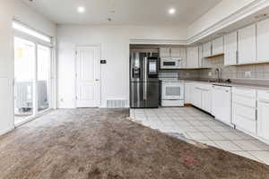 Kitchen featuring white cabinets, white appliances, decorative backsplash, light tile patterned floors, and recessed lighting