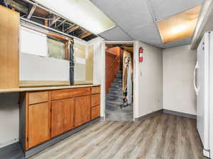 Finished below grade area with stairs, light wood finished floors, freestanding refrigerator, and a paneled ceiling