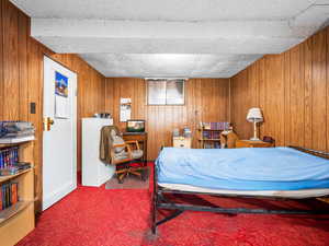 Carpeted bedroom with wooden walls and a textured ceiling