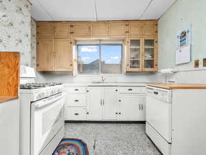 Kitchen featuring white appliances, glass insert cabinets, dark speckled floor, wooden counters, and white cabinets