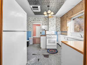 Kitchen with white appliances, light countertops, decorative light fixtures, a chandelier, and backsplash