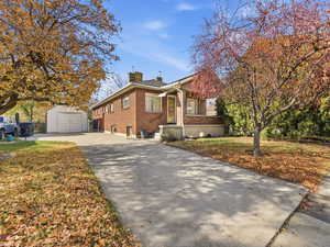 View of property exterior with brick siding, asphalt driveway, a chimney, and a storage shed