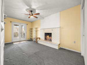 Unfurnished living room featuring a fireplace, dark colored carpet, french doors, wooden walls, and a ceiling fan