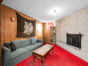 Carpeted living area featuring a fireplace, wood walls, and a textured ceiling