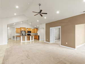 Unfurnished living room with light carpet, ceiling fan, arched walkways, recessed lighting, and high vaulted ceiling