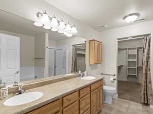 Bathroom with a walk in closet, a stall shower, double vanity, light tile patterned flooring, and light colored carpet
