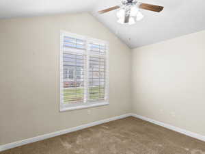 Carpeted empty room featuring vaulted ceiling and a ceiling fan