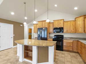Kitchen featuring black appliances, light tile patterned floors, decorative light fixtures, a center island, and light brown cabinetry