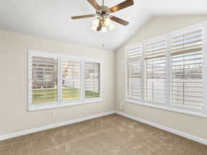 Carpeted spare room featuring vaulted ceiling and ceiling fan