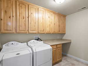 Laundry room with washer and dryer, a textured ceiling, light tile patterned floors, and cabinet space