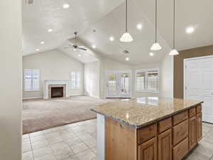 Kitchen featuring hanging light fixtures, light stone countertops, brown cabinets, light tile patterned floors, and light colored carpet