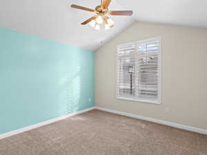 Carpeted spare room with ceiling fan and vaulted ceiling