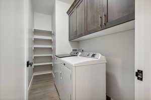 Washroom with cabinet space, light wood-type flooring, and washer and clothes dryer