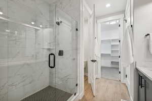 Bathroom featuring vanity, light wood-type flooring, a marble finish shower, a walk in closet, and recessed lighting