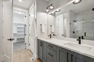 Bathroom with double vanity, a marble finish shower, light wood-type flooring, and a spacious closet