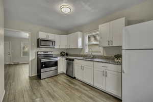 Kitchen with stainless steel appliances, white cabinetry, light wood finished floors, and light stone countertops