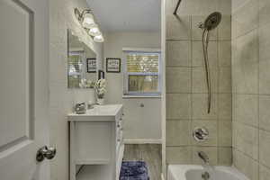 Full bath with bathing tub / shower combination, light wood-style flooring, a textured wall, and vanity