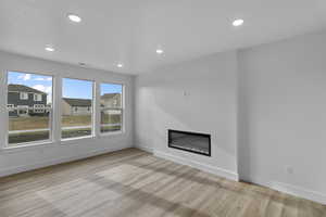 Unfurnished living room with a glass covered fireplace, light wood-style floors, recessed lighting, and a residential view