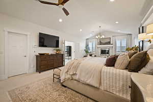 Carpeted bedroom with vaulted ceiling, a chandelier, ceiling fan, recessed lighting, and a glass covered fireplace