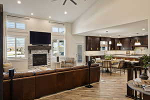 Living room featuring recessed lighting, light wood-type flooring, high vaulted ceiling, a ceiling fan, and a stone fireplace