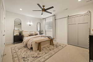 Bedroom with a barn door, light carpet, recessed lighting, and ceiling fan