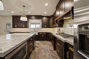 Kitchen featuring dark brown cabinetry, stainless steel appliances, tasteful backsplash, recessed lighting, and light stone countertops