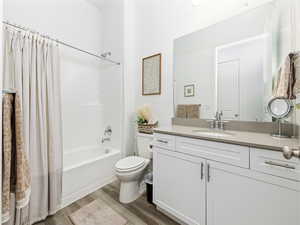 Full bathroom with shower / bathtub combination with curtain, dark wood-type flooring, and vanity