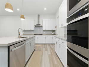 Kitchen with stainless steel appliances, decorative backsplash, light wood-style floors, hanging light fixtures, and white cabinets