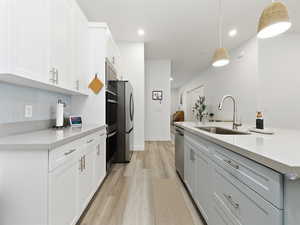 Kitchen featuring hanging light fixtures, light wood-style flooring, a center island with sink, stainless steel appliances, and light stone countertops