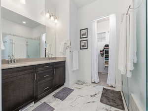 Full bathroom with a spacious closet, a shower stall, double vanity, and light marble finish floors
