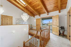 Beautiful architectural detail. Hall featuring an upstairs landing, wood ceiling, a skylight, carpet floors, and a chandelier