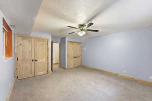 Basement Bedroom #1  with light colored carpet, a textured ceiling, ceiling fan, and multiple closets